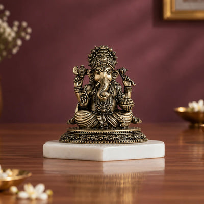 Brass sitting Ganesha murti holding a modak bowl, on a white marble base