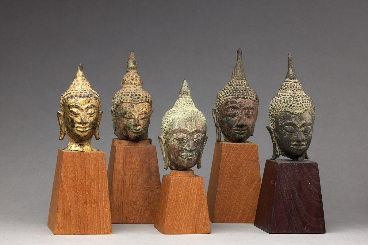 Five Thai bronze Buddha heads on wooden stands, each with rows of tight curls and a raised ushnisha