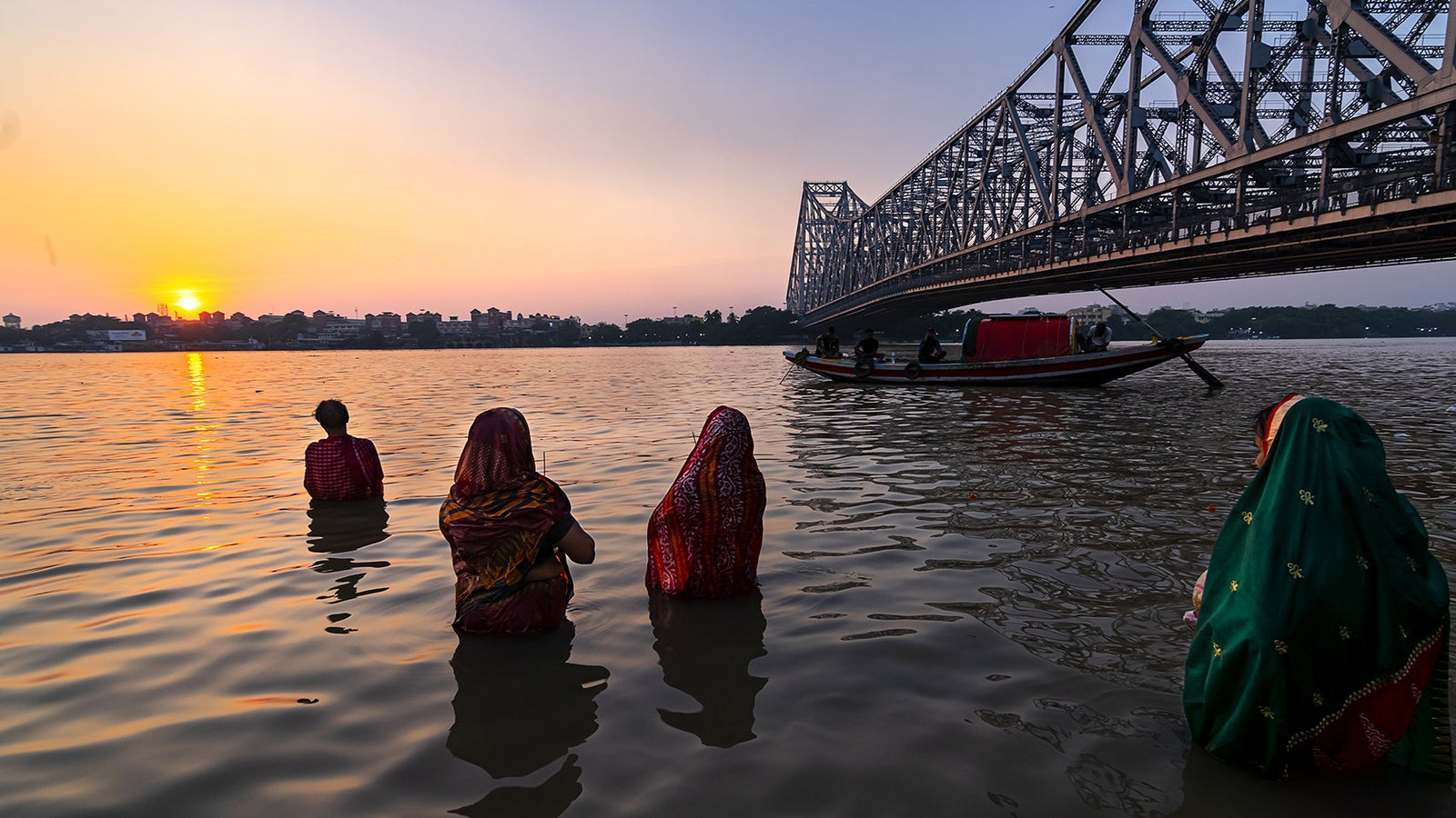 Women stand in the river at Chhath, facing the low sun beside the Howrah Bridge.