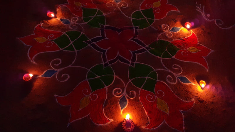 A Diwali rangoli in red and green drawn on the floor and ringed with small lit clay diyas at night.