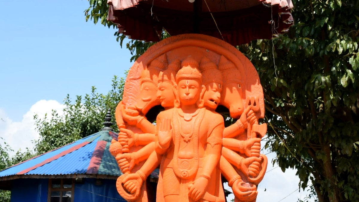A saffron-painted Panchmukhi Hanuman statue with five faces and many arms standing under a canopy