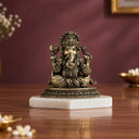 Brass sitting Ganesha murti holding a modak bowl, on a white marble base